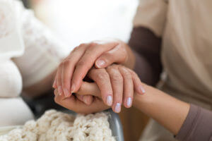 Hospice home health care aide holding the hand of her elderly patient.