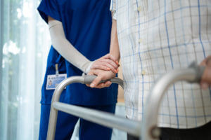 An image close-up of a nurse helping a man walk with a walker in a nursing home after hip replacement surgery.