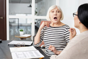 A focused female senior tutor demonstrates pronunciation during in-home speech therapy.