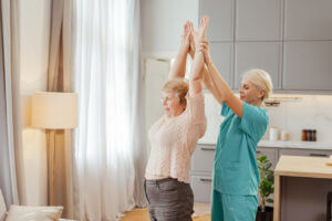 A nurse assists a senior woman in stretching her arms during outpatient physical therapy at home.