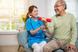 A young physiotherapist is assisting an elderly man with lifting a dumbbell during in-home physical therapy for seniors.