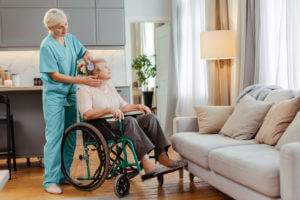 A nurse is brushing the hair of a senior woman in a wheelchair at home while providing care for a disabled person.
