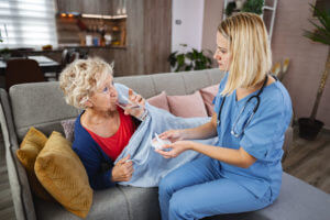 A caring private nurse assists elderly woman with medication at home during day.