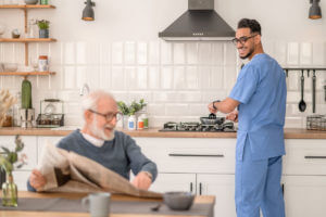 A cheerful male caregiver is preparing breakfast for an elderly man during home senior care services.