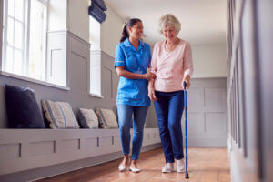 A senior woman at home using a walking stick during nursing care services for recovery after surgery.