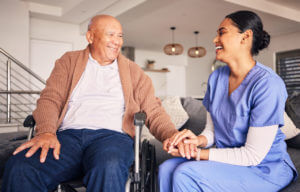 Happy nurse helping man in wheelchair during nursing care services at home.