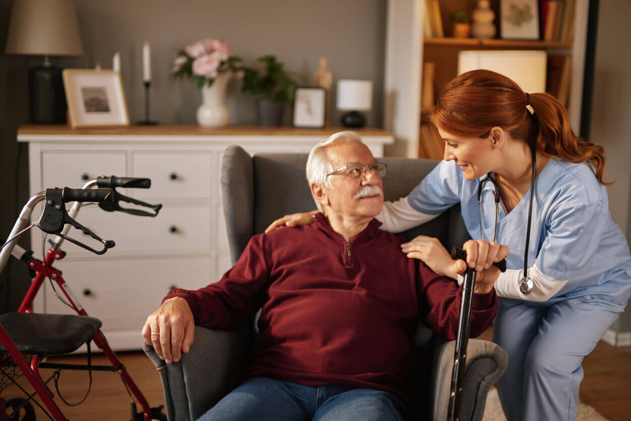 Nurse assisting elderly man at home with walking cane during stroke rehabilitation.