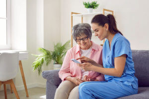 A nurse providing skilled nursing care at home, shows an elderly woman a photo on a mobile phone.