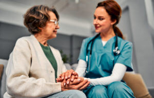 Female nurse hold her senior dementia patient's hand during hospice care.