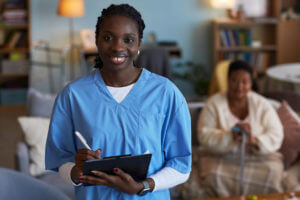 Image of Smiling Black Female Nurse with Clipboard during Patient Visit For An Outpatient Physical Therapy.